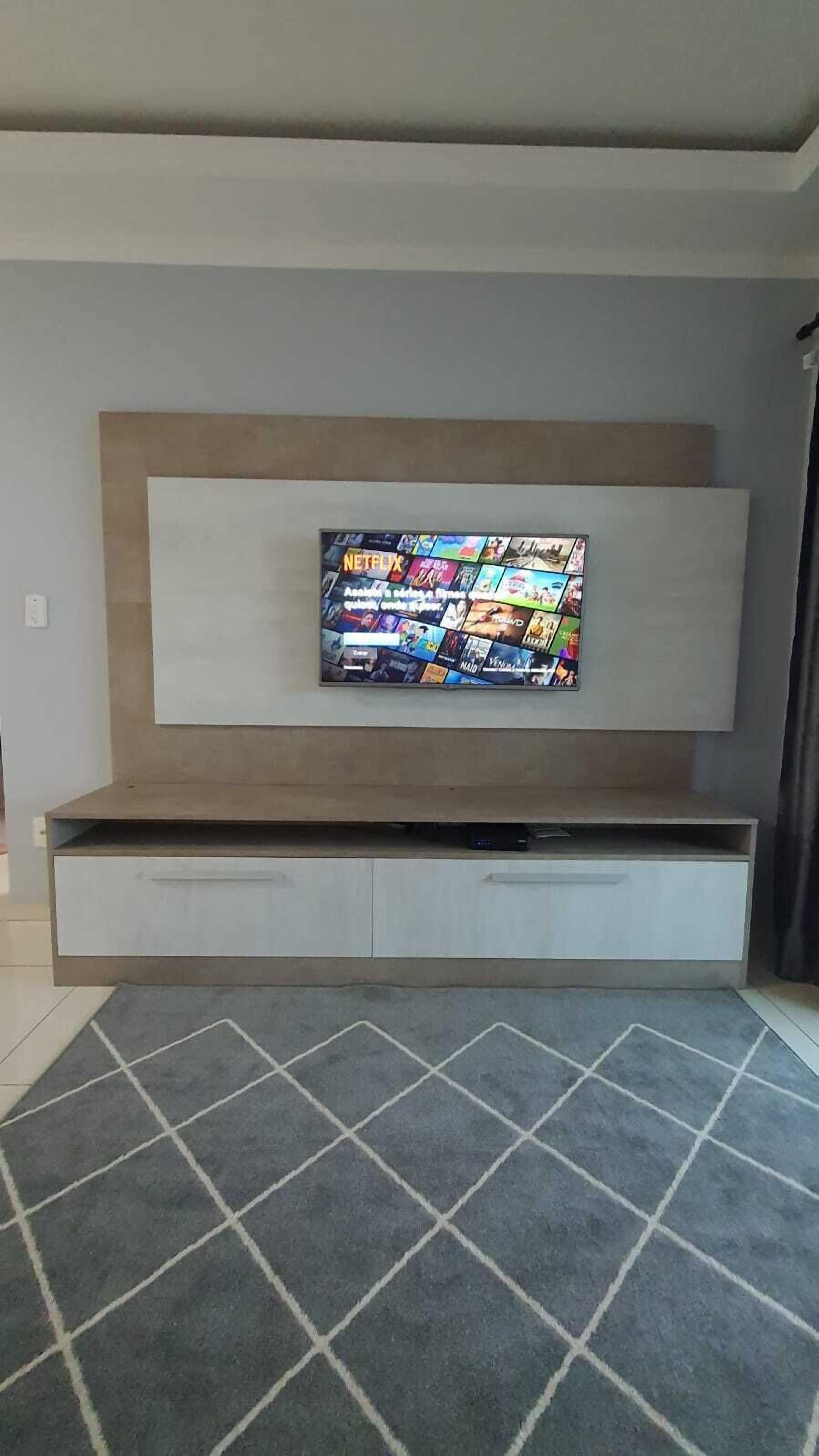 Un salon moderne avec un téléviseur à écran plat fixé à un meuble en bois, un tapis à motifs gris et un mur blanc.
