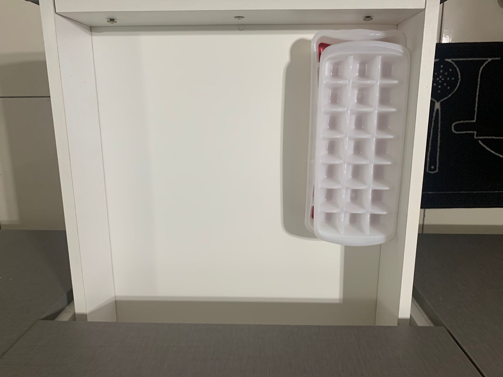 A white ice cube tray hanging from a white cabinet.