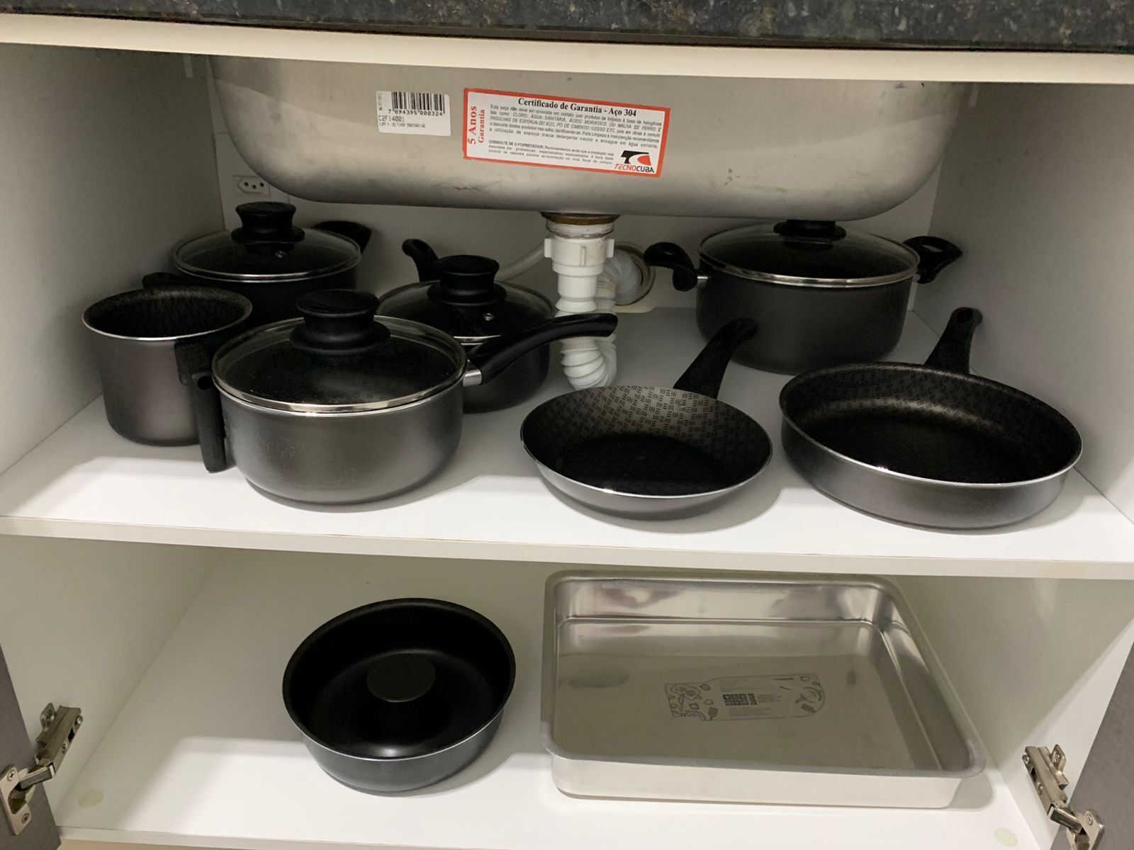 A kitchen shelf with various cookware including pots, pans, and a baking tray.