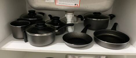 A kitchen shelf with various cookware including pots, pans, and a baking tray.