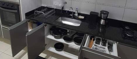 A modern kitchen with white cabinets, a black countertop, a microwave, a sink, and a coffee maker.