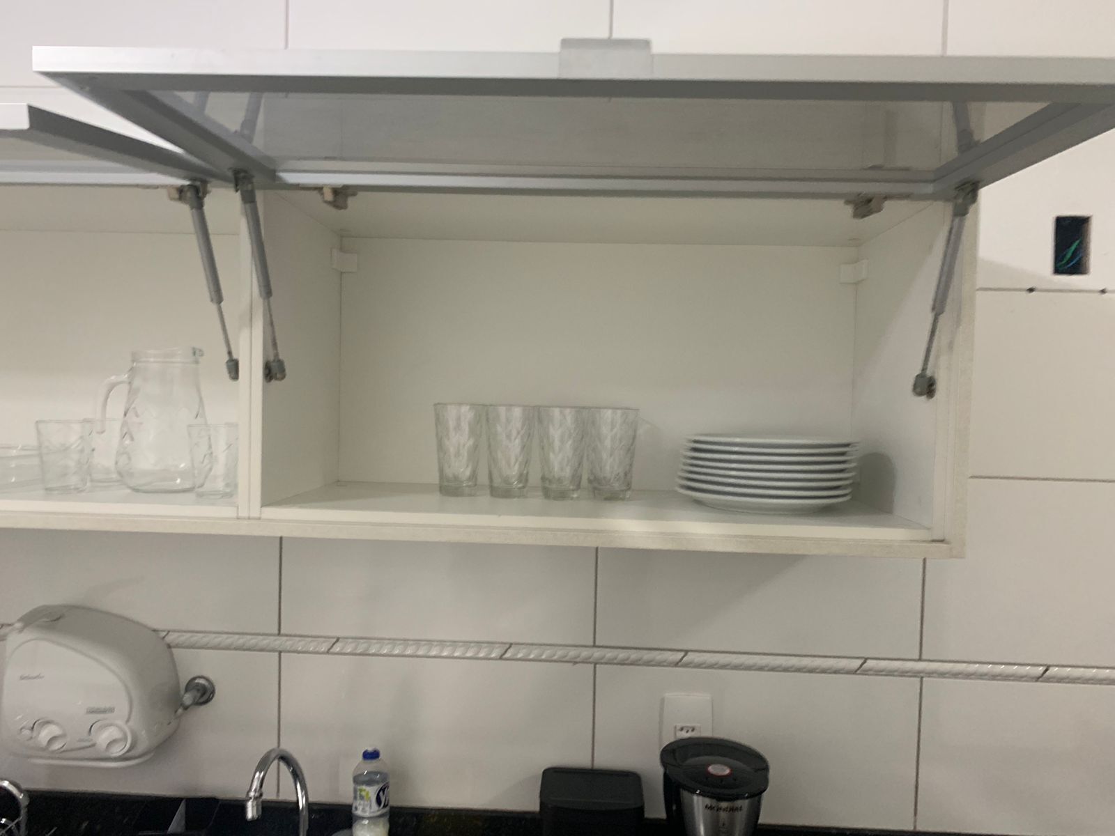 Et køkken med en hvid bordplade, vask, elkedel, vandflaske og en blender.