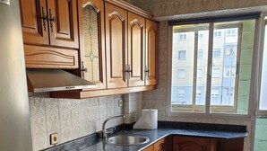 Een keuken met houten kastjes, een roestvrijstalen spoelbak, een fornuis en vloertegels met een patroon.