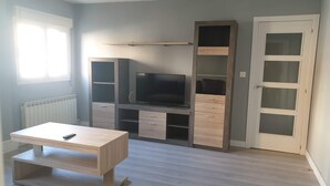 Een kamer met een televisie op een houten standaard, een tafel en een kast met lades.