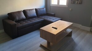 Een moderne woonkamer met een donkerbruine hoekbank, een houten salontafel en een raam met zonwering.