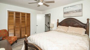 A bedroom with a bed, a ceiling fan, a wooden headboard, a nightstand, a lamp, a chair, and a closet with sliding doors. - A Taste of Tennessee (Knoxville, TN)