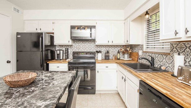 A modern kitchen with white cabinets, a black refrigerator, a stove, and a sink. - A Taste of Tennessee (Knoxville, TN)