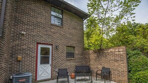 A brick building with a door, windows, and a patio area with three chairs and a trash bin. - A Taste of Tennessee (Knoxville, TN)