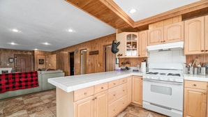 A kitchen with wooden cabinets, a white stove, and a tiled floor. - HOT TUB! GAME ROOM w/LEDs! CLOSE TO EVERYTHING! EV Charger! Adorable décor. (Big Bear City)