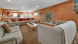 A cozy living room with a fireplace, wooden walls, and a dining area in the background. - HOT TUB! GAME ROOM w/LEDs! CLOSE TO EVERYTHING! EV Charger! Adorable décor. (Big Bear City)