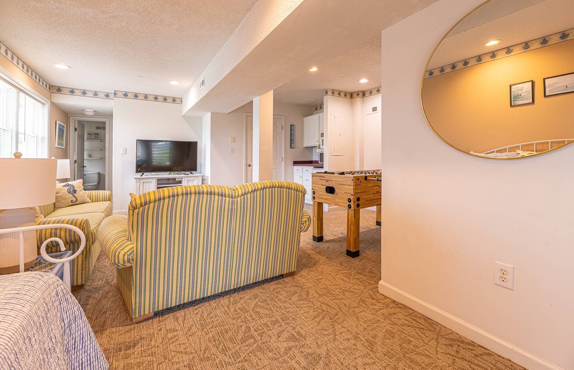 A living room with striped sofas, a television, and a foosball table.