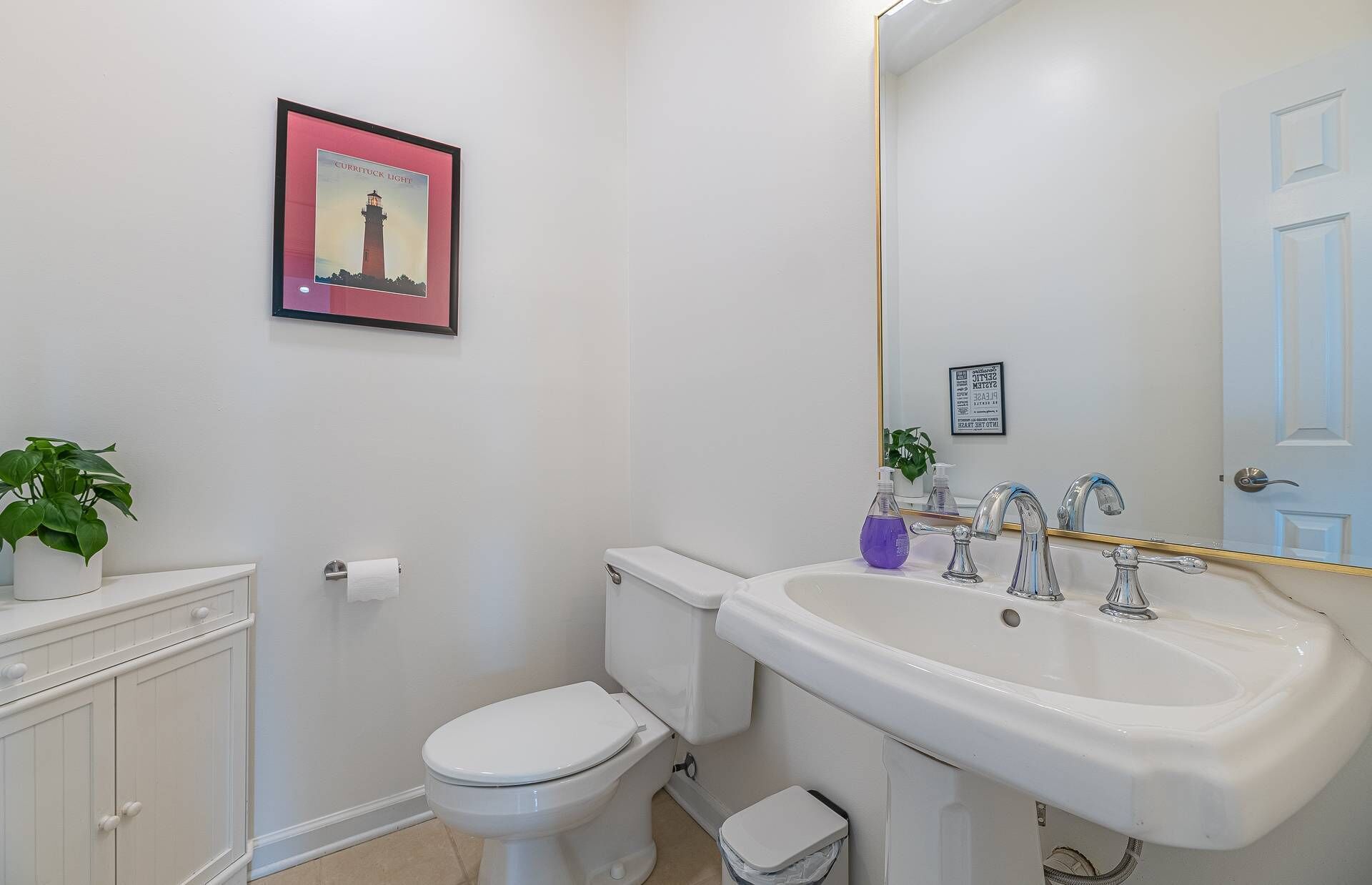 Une salle de bain équipée de toilettes, d’un lavabo et d’un tableau représentant un phare.