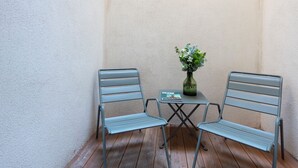 En liten uteplats med två metallstolar och ett bord, en vas med blommor och en bok som ligger på bordet.