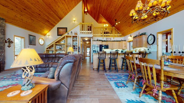 A spacious living room with a leather couch, wooden dining table, and a staircase leading to an upper level. - Pets | Fireplace | Large Deck | Casa Arriba (Angel Fire)
