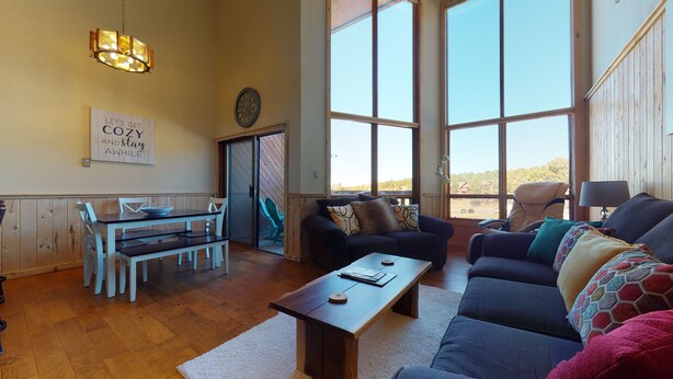 A cozy living room with a dining area, large windows, and a view of the outdoors.