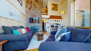A modern living room with a stone wall, a fireplace, and a kitchen in the background.