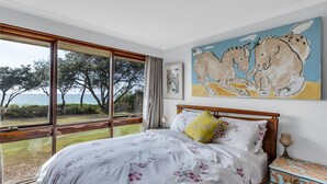 Ein Schlafzimmer mit großem Fenster und Blick auf eine schöne Landschaft, einem Bett mit floralem Bettzeug und einem Gemälde von Pferden an der Wand.