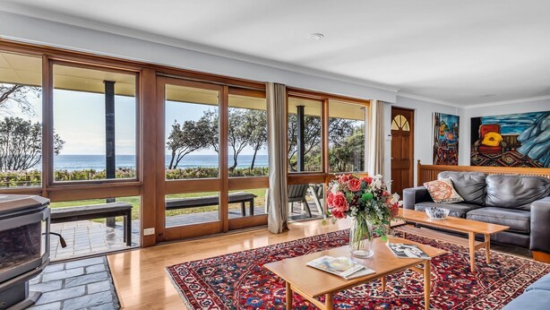 Ein geräumiges Wohnzimmer mit einem großen Schiebeglastür, die auf eine Terrasse mit Meerblick führt. Es gibt ein Ledersofa, einen Couchtisch mit Blumenvase und ein Bild an der Wand.