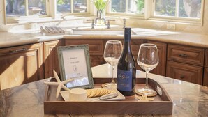 Un plateau en bois avec une bouteille de vin, des verres, une pancarte d’accueil encadrée, des étoiles de mer et des crackers, le tout posé sur un comptoir de cuisine.
