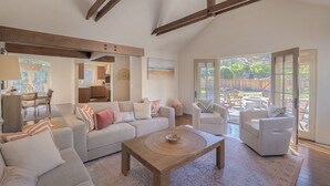 Un vaste salon comprenant un grand canapé, une table basse et un coin repas avec une table et des chaises. Une grande fenêtre offre une vue sur le jardin arrière.
