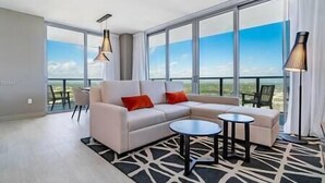 A modern living room with a sectional sofa, a round coffee table, and a view of the outdoors through large windows. - 2402 Hyde House Ocean View 2 Be 2 Ba, Special Amenities (Hollywood)