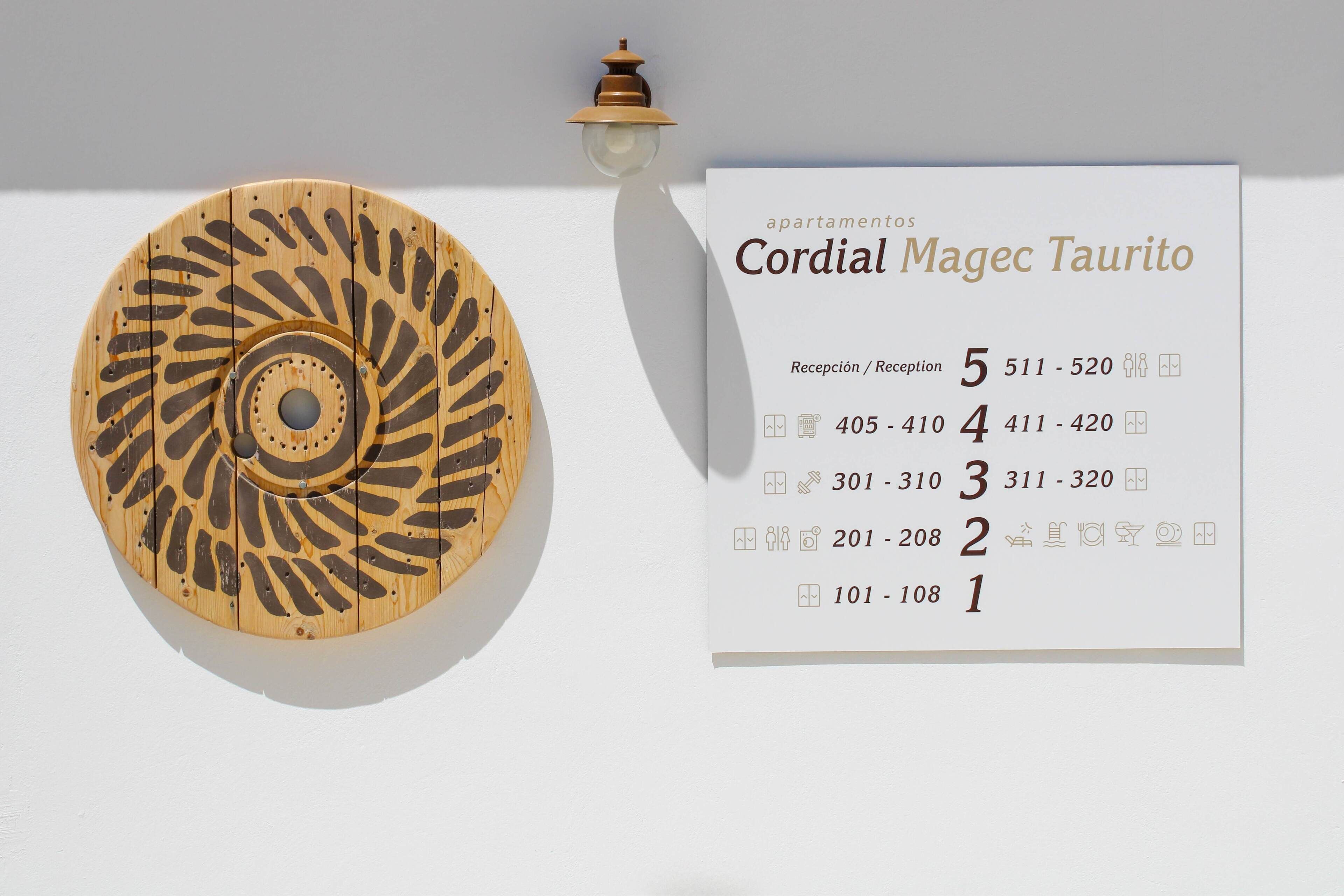 A wall-mounted wooden decorative piece with a circular pattern and a sign listing apartment numbers and reception phone numbers.