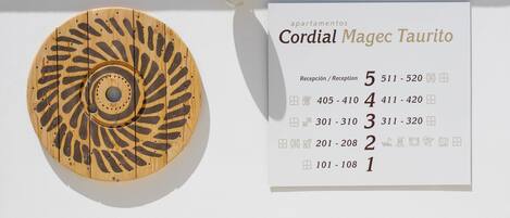 A wall-mounted wooden decorative piece with a circular pattern and a sign listing apartment numbers and reception phone numbers.