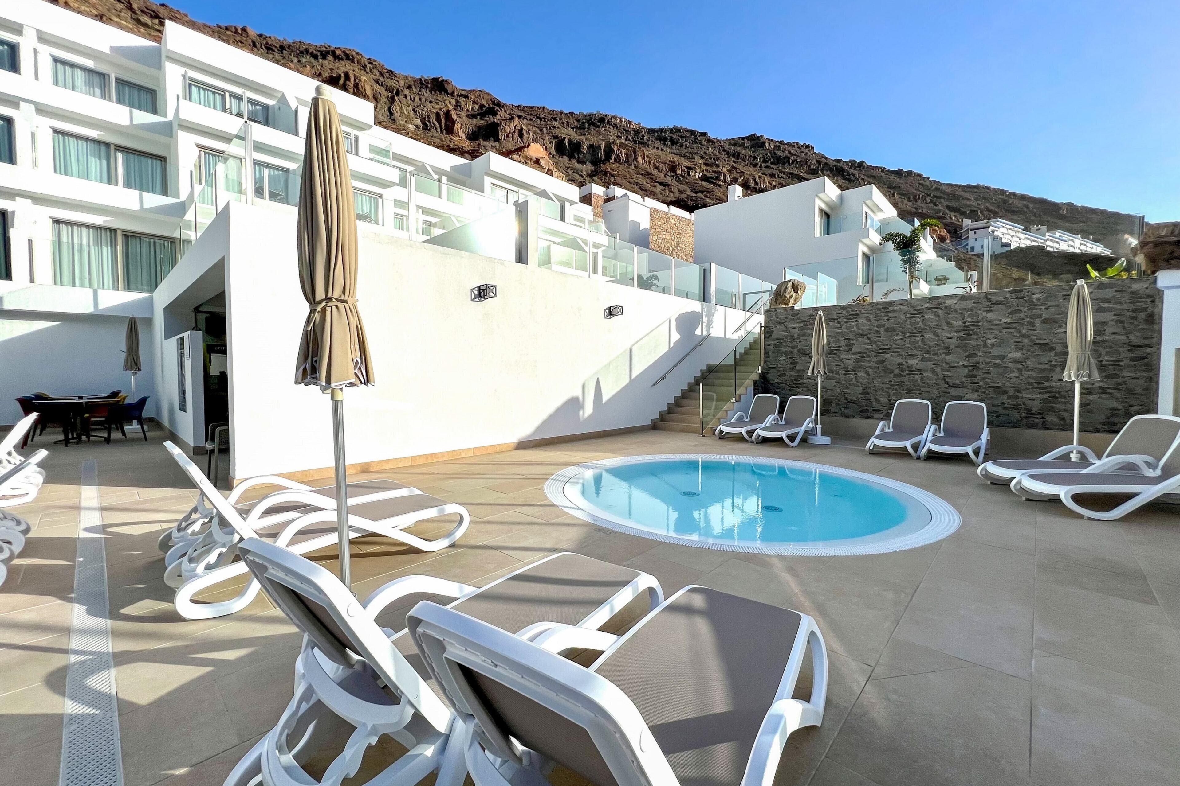 Un'area piscina con lettini, una piccola piscina e una scala che conduce a un edificio con diverse finestre.