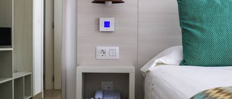 Habitación de hotel con cama, mesita de noche con lámpara, termostato y teléfono.