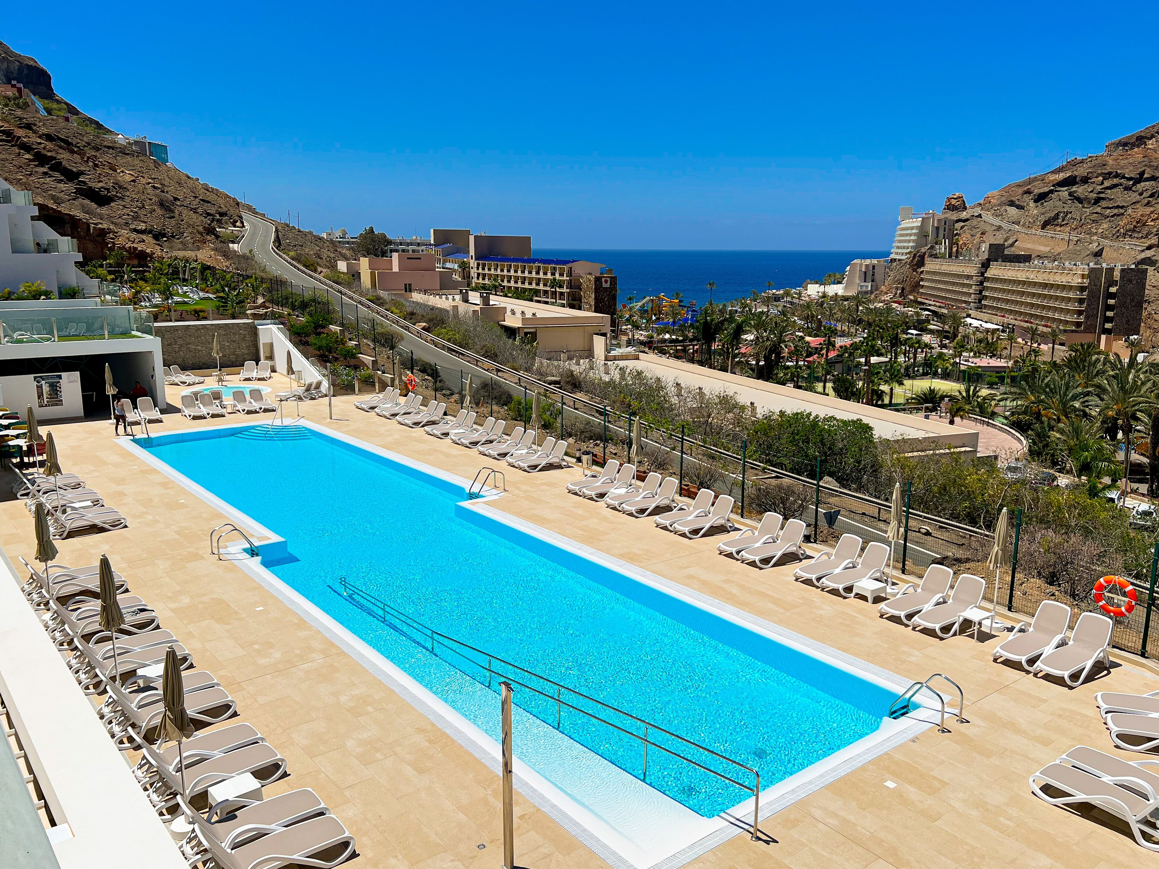 Piscina de resort con tumbonas y vista al océano.