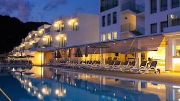 Un hôtel moderne doté d’un espace de détente au bord de la piscine, de plusieurs balcons et dont l’image se reflète dans l’eau de la piscine.