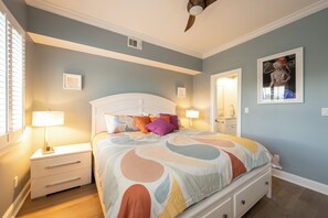 A bedroom with a bed, nightstands, a ceiling fan, and artwork on the walls.