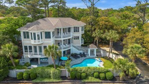 A multi-story house with a pool, surrounded by lush greenery and palm trees.