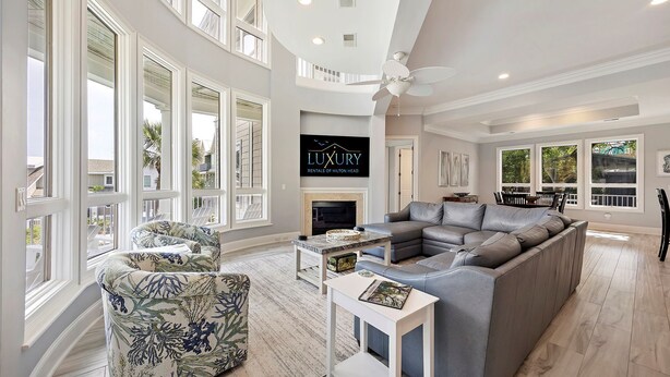 A spacious living room with large windows, a fireplace, and a ceiling fan.