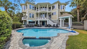 A large house with a swimming pool, a covered patio, and a staircase leading to a balcony.