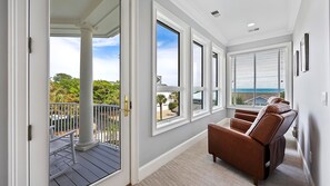 Quarto com varanda, janelas amplas, uma poltrona de couro marrom e vista para o oceano.