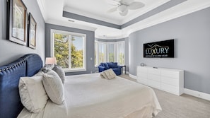 Une chambre à coucher avec un grand lit, un canapé bleu, une commode blanche et un ventilateur de plafond.