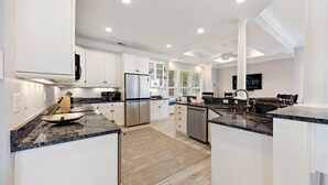 A modern kitchen with white cabinetry, granite countertops, stainless steel appliances, and a view of greenery outside.
