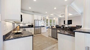 A modern kitchen with white cabinetry, granite countertops, stainless steel appliances, and a view of greenery outside.
