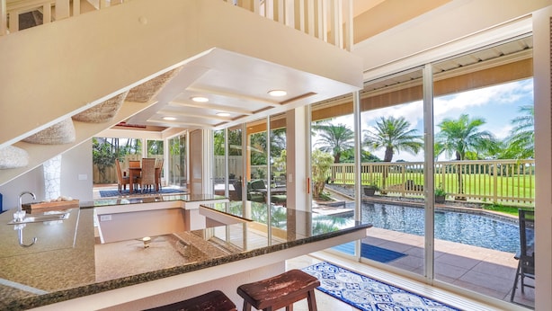 Una cocina moderna con una isla grande, un área de comedor con paredes de vidrio y vistas a una piscina y jardín.