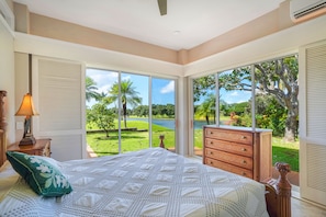 A bedroom with a large bed, a dresser, and a view of a lush garden and lake.