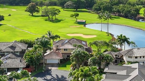 Campo de golf con un obstáculo acuático, rodeado de casas residenciales con techos inclinados.