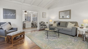 A spacious living room with a high ceiling, a grey sofa, a wooden bench, a coffee table, and a patterned rug.