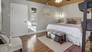 A bedroom with a bed, bench, ceiling fan, and a door.