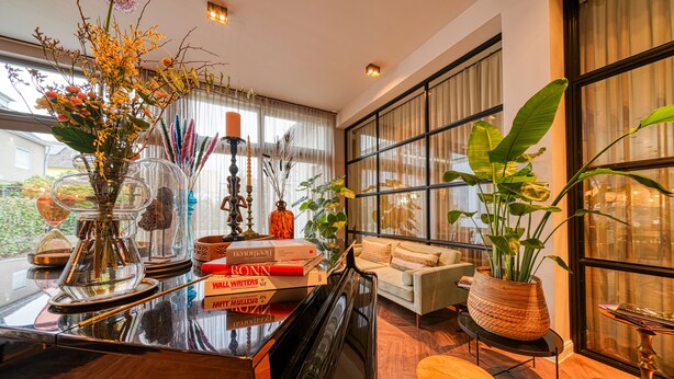 Un salón luminoso con un piano, libros y plantas decorativas.
