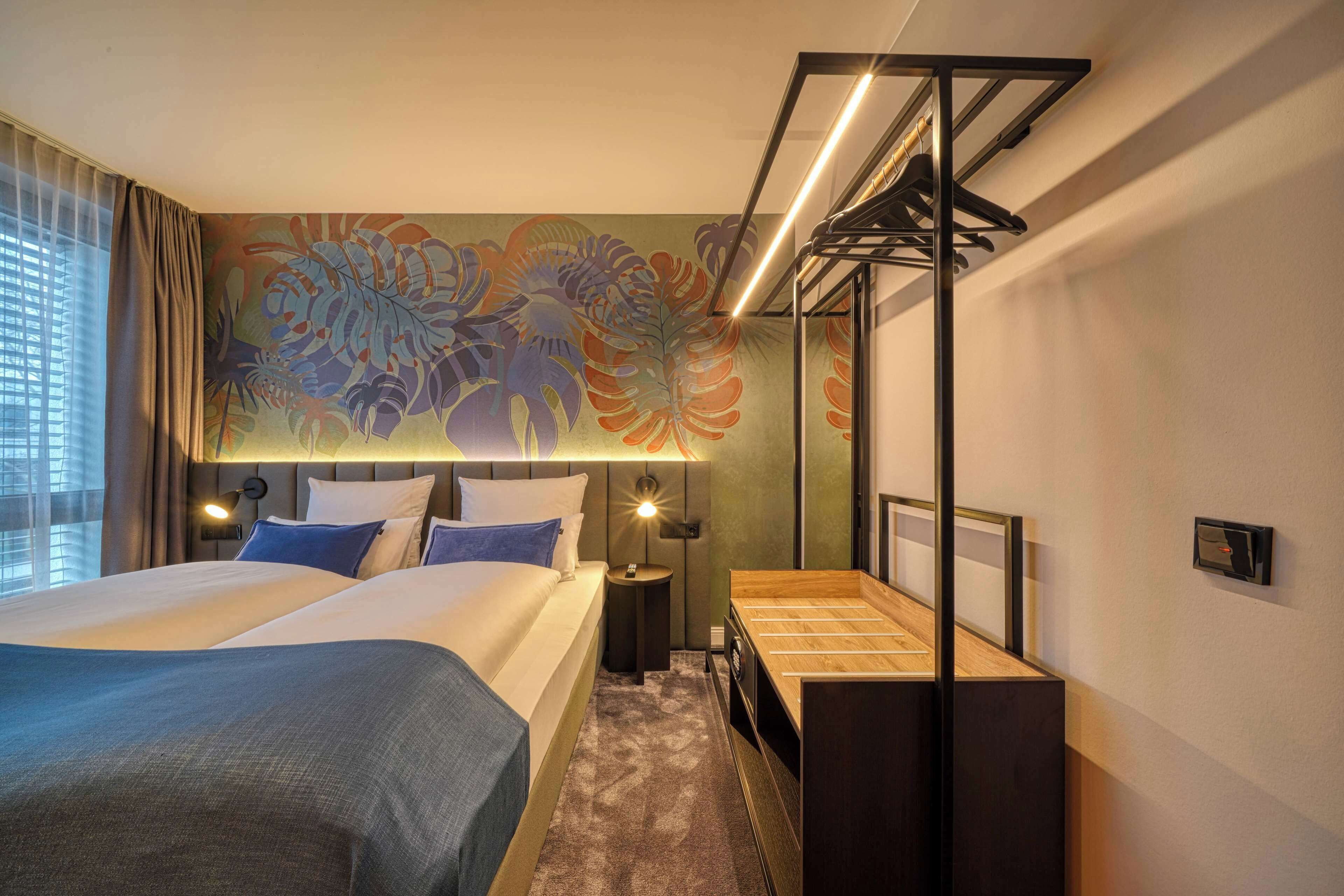 Habitación de hotel con una cama grande, un escritorio, un espejo y una pared con un mural floral.