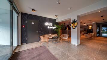 A modern hotel lobby with a reception desk, seating area, and a large plant.