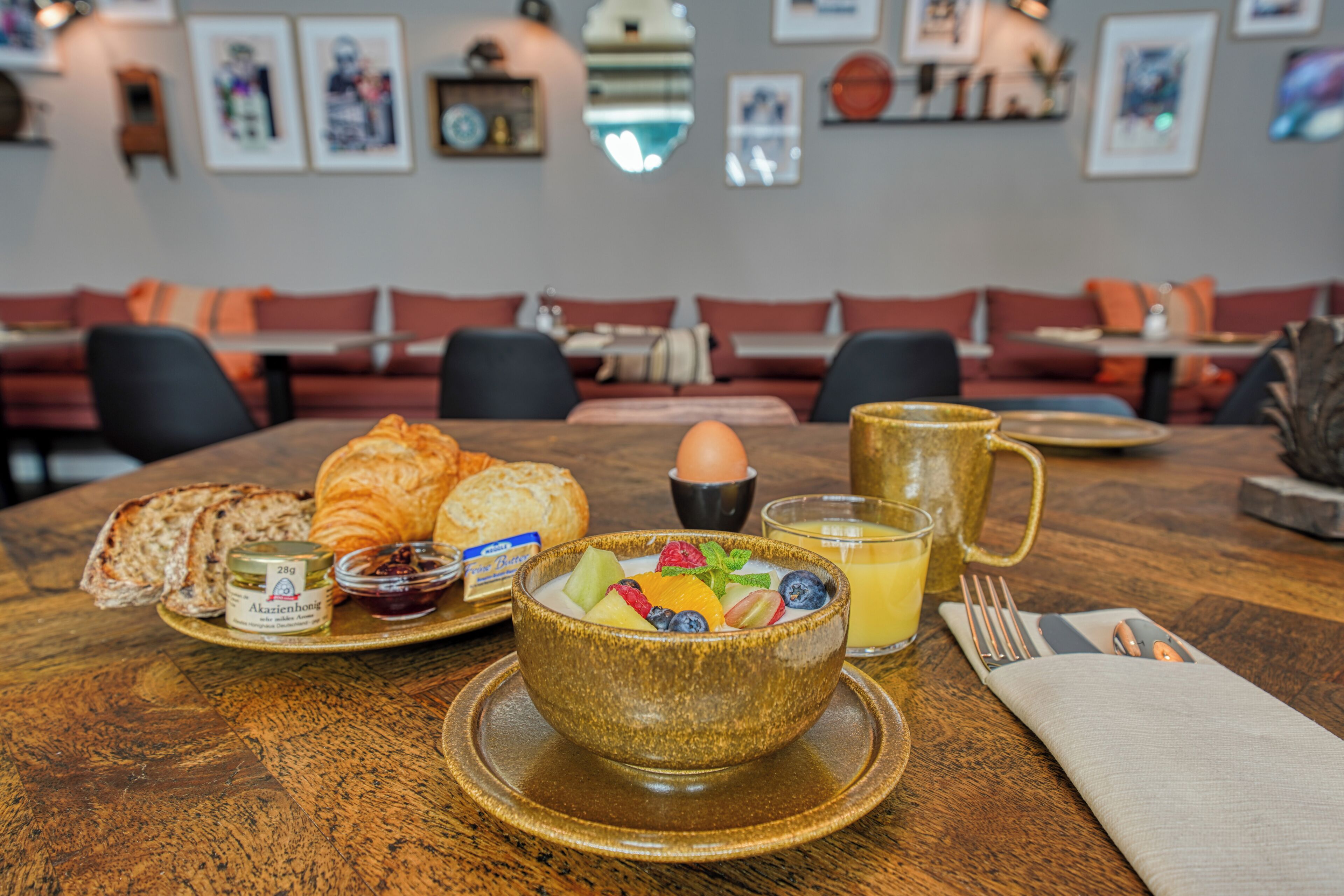 A breakfast setting with croissants, a bowl of fruit, a glass of orange juice, and a mug on a wooden table.