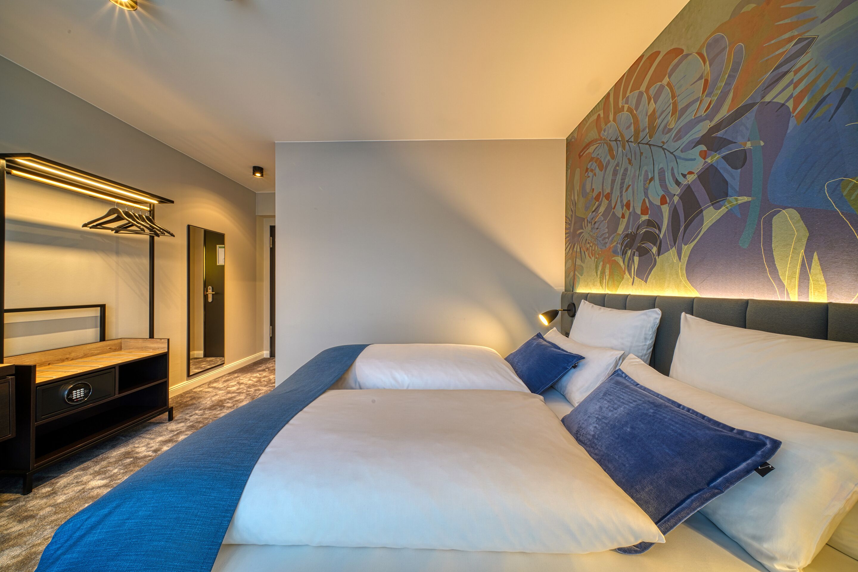 Een hotelkamer met een groot bed, een nachtkastje, een kledingkast en een wandlamp.