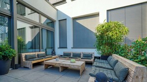 Un área de estar al aire libre moderna con mobiliario de madera y una planta grande en maceta.